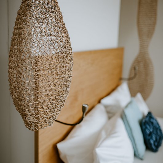 Übernachten am Bostalsee: Seezeitlodge Hotel & Spa Geflochtene Hängelampe über Holz-Kopfteil und Kissen auf dem Bett