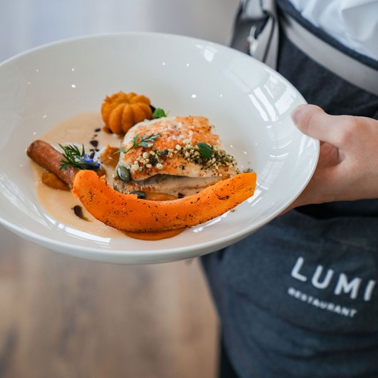LUMI: our restaurant at Lake Bostalsee Person holding plate with gourmet fish and pumpkin dish