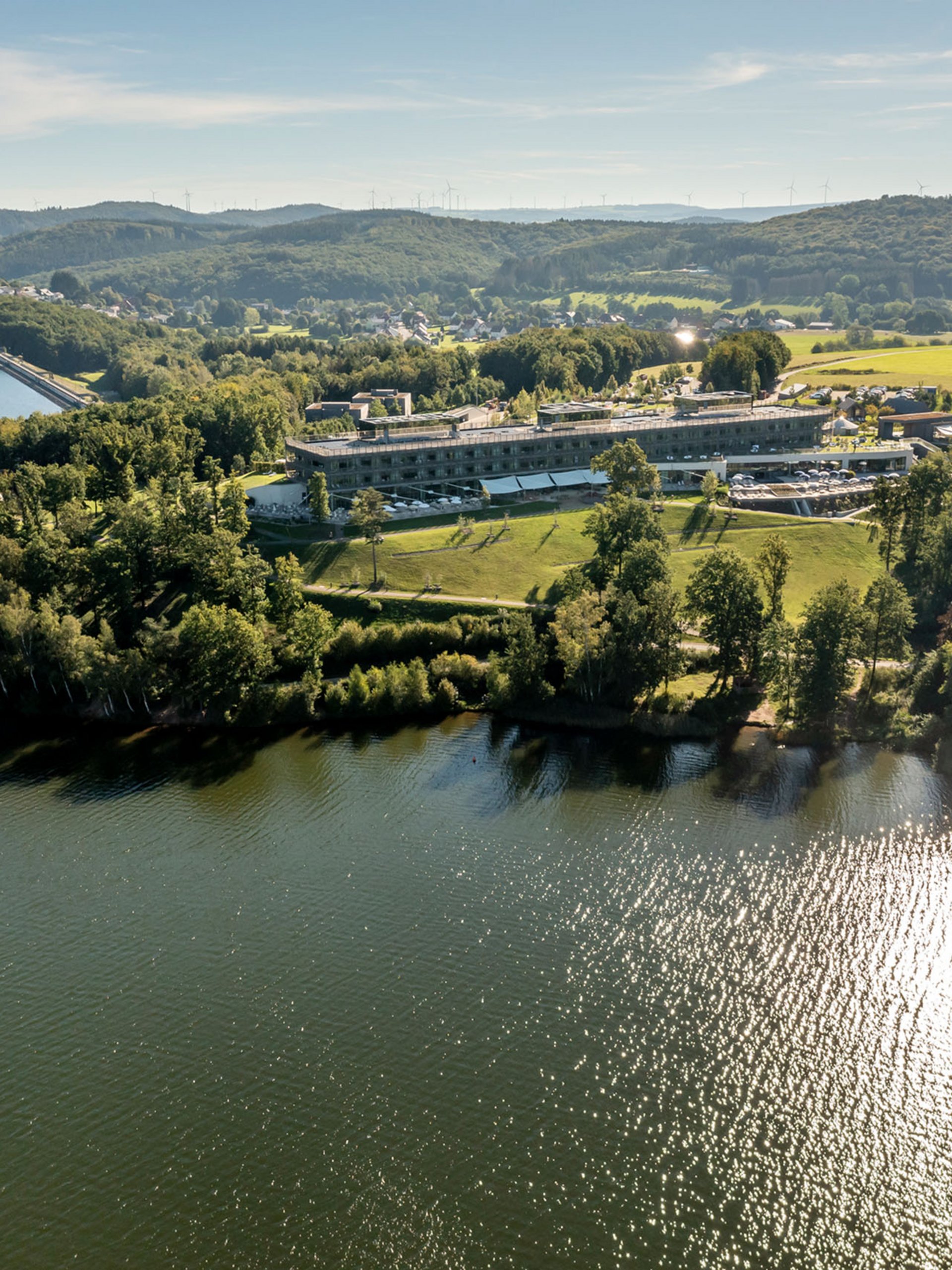 Seezeitlodge : Galerie photos Vue aérienne d'un lac avec un bâtiment et des collines boisées en arrière-plan