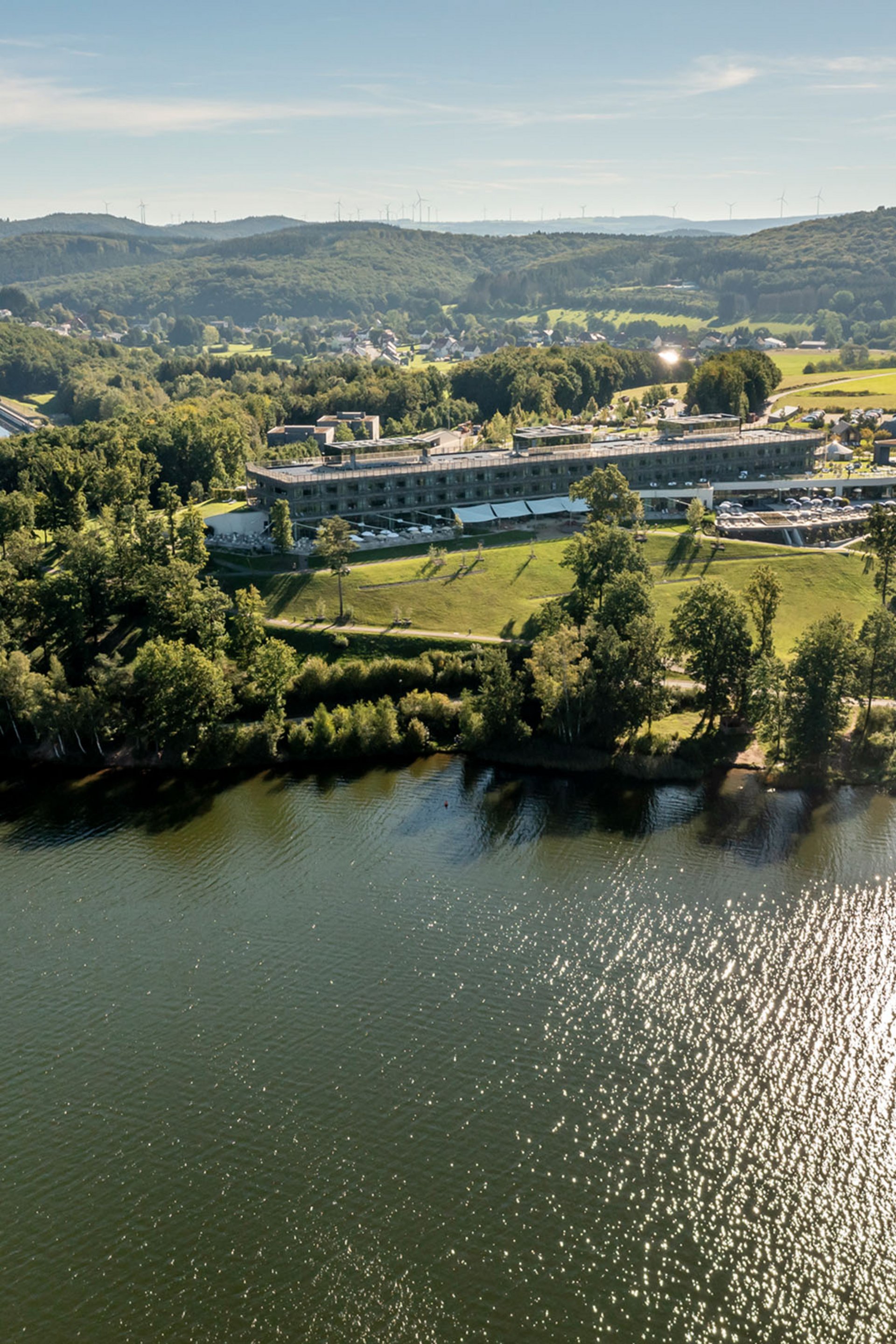 Seezeitlodge: Bildergalerie Luftaufnahme von einem See mit einem Gebäude und bewaldeten Hügeln im Hintergrund