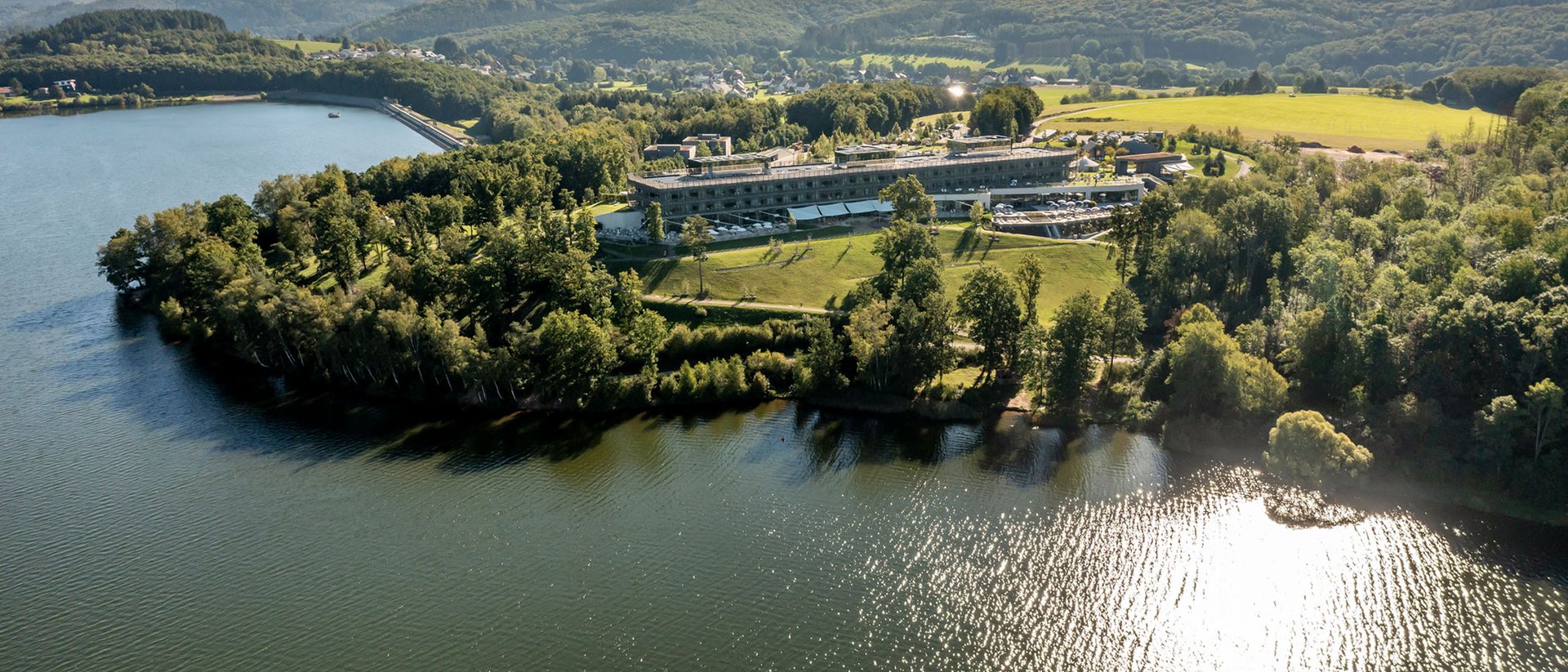 Seezeitlodge: Bildergalerie Luftaufnahme von einem See mit einem Gebäude und bewaldeten Hügeln im Hintergrund
