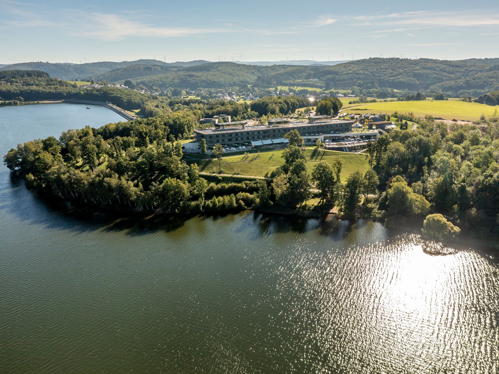 Seezeitlodge: Bildergalerie Luftaufnahme von einem See mit einem Gebäude und bewaldeten Hügeln im Hintergrund