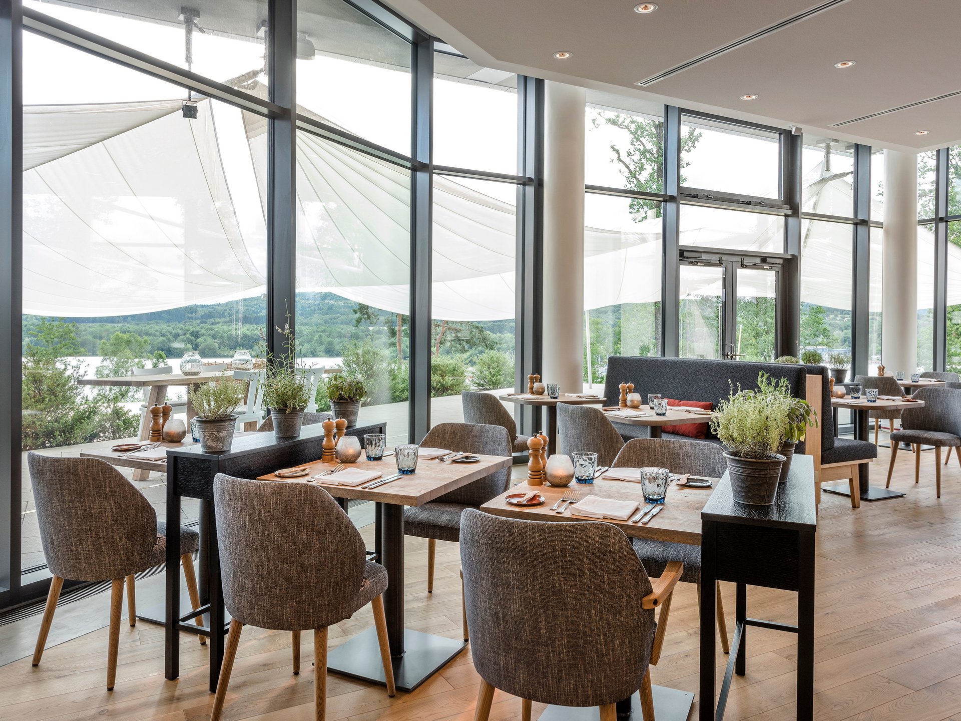 Seezeitlodge : Galerie photos Salle de restaurant moderne avec parquet, tables et chaises, grandes fenêtres et vue