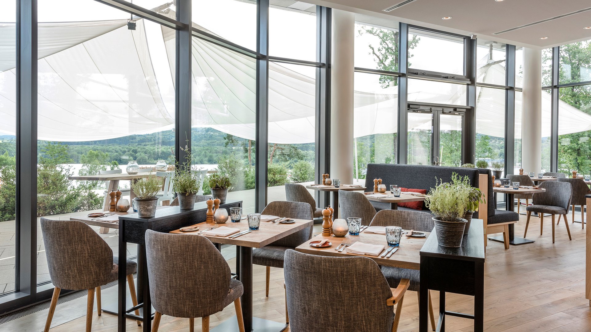 Seezeitlodge: Bildergalerie Moderner Restaurantbereich mit Holzboden, Tischen und Stühlen, großer Fensterfront und Aussicht