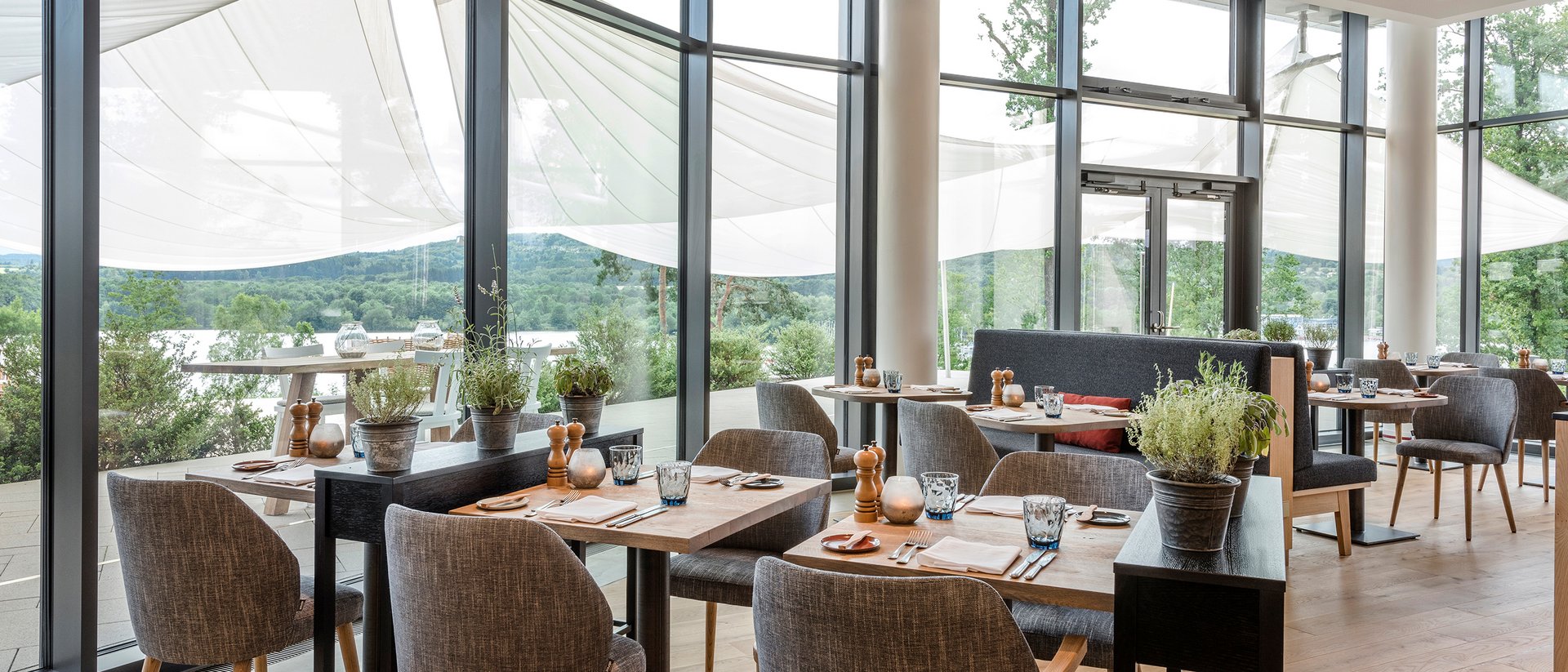 Seezeitlodge: Bildergalerie Moderner Restaurantbereich mit Holzboden, Tischen und Stühlen, großer Fensterfront und Aussicht