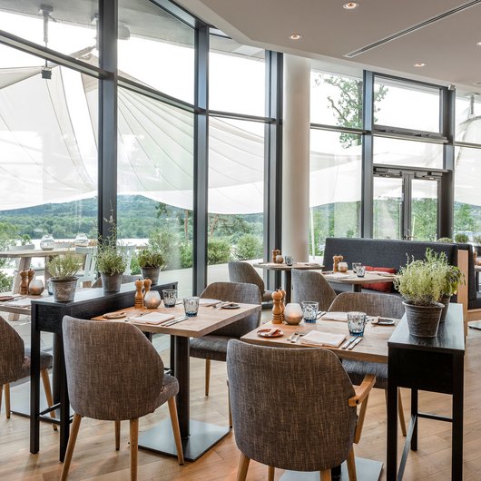Ihr Genusshotel am Bostalsee Moderner Restaurantbereich mit Holzboden, Tischen und Stühlen, großer Fensterfront und Aussicht