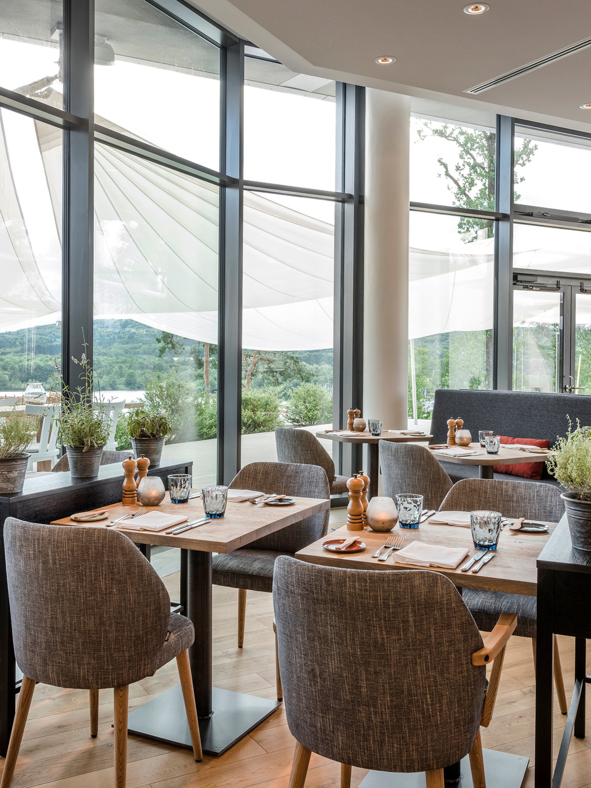 Seezeitlodge : Galerie photos Salle de restaurant moderne avec parquet, tables et chaises, grandes fenêtres et vue