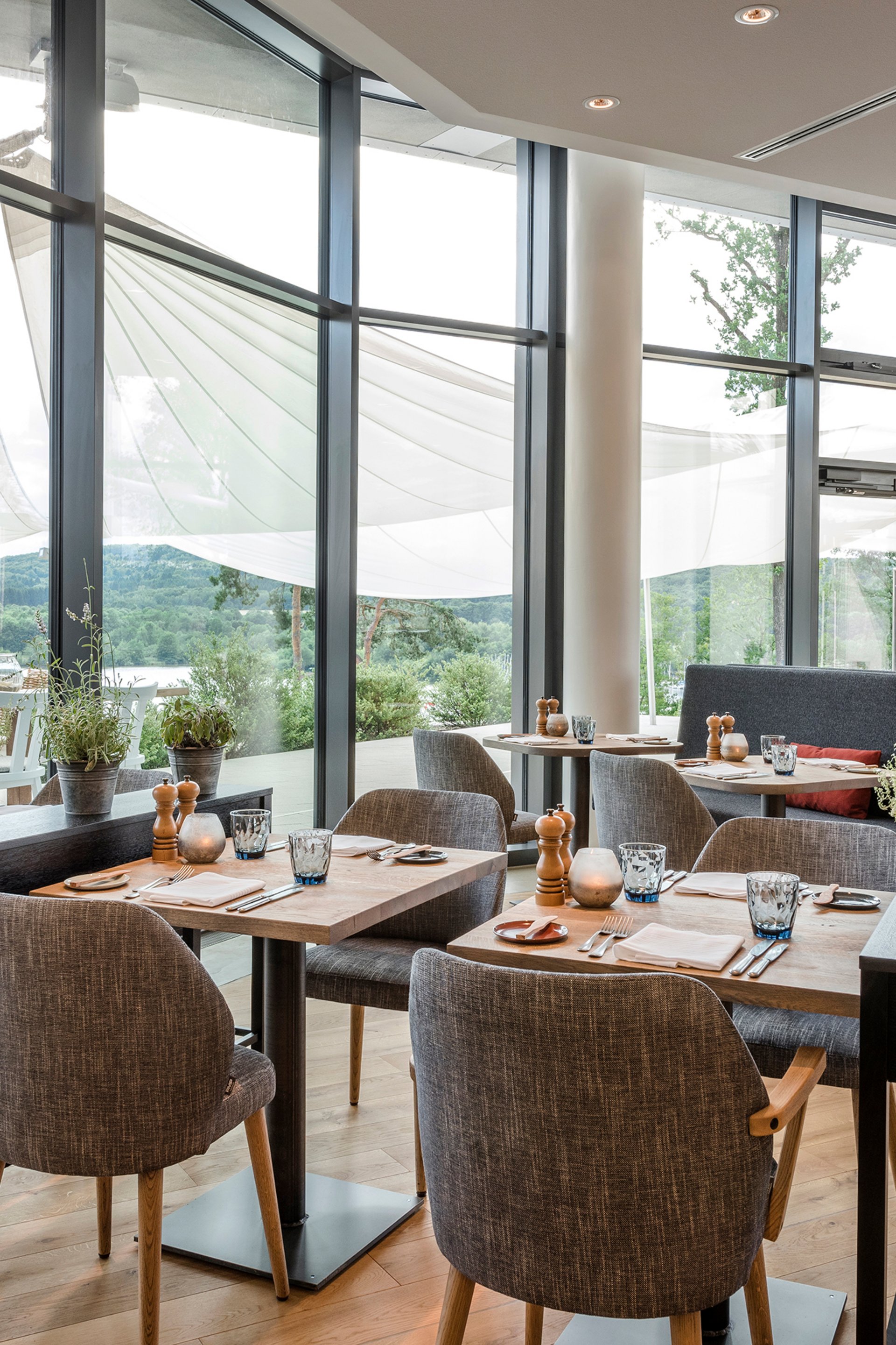 Seezeitlodge : Galerie photos Salle de restaurant moderne avec parquet, tables et chaises, grandes fenêtres et vue