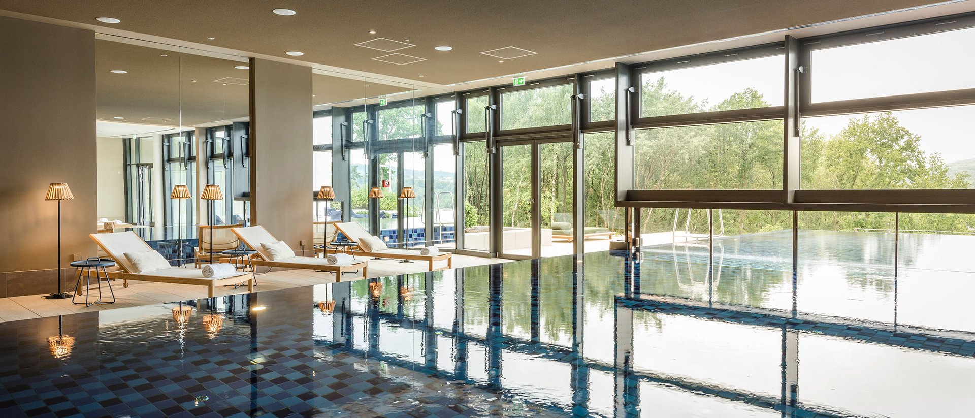 Seezeitlodge : Galerie photos Piscine intérieure avec chaises longues et grandes fenêtres donnant sur la nature