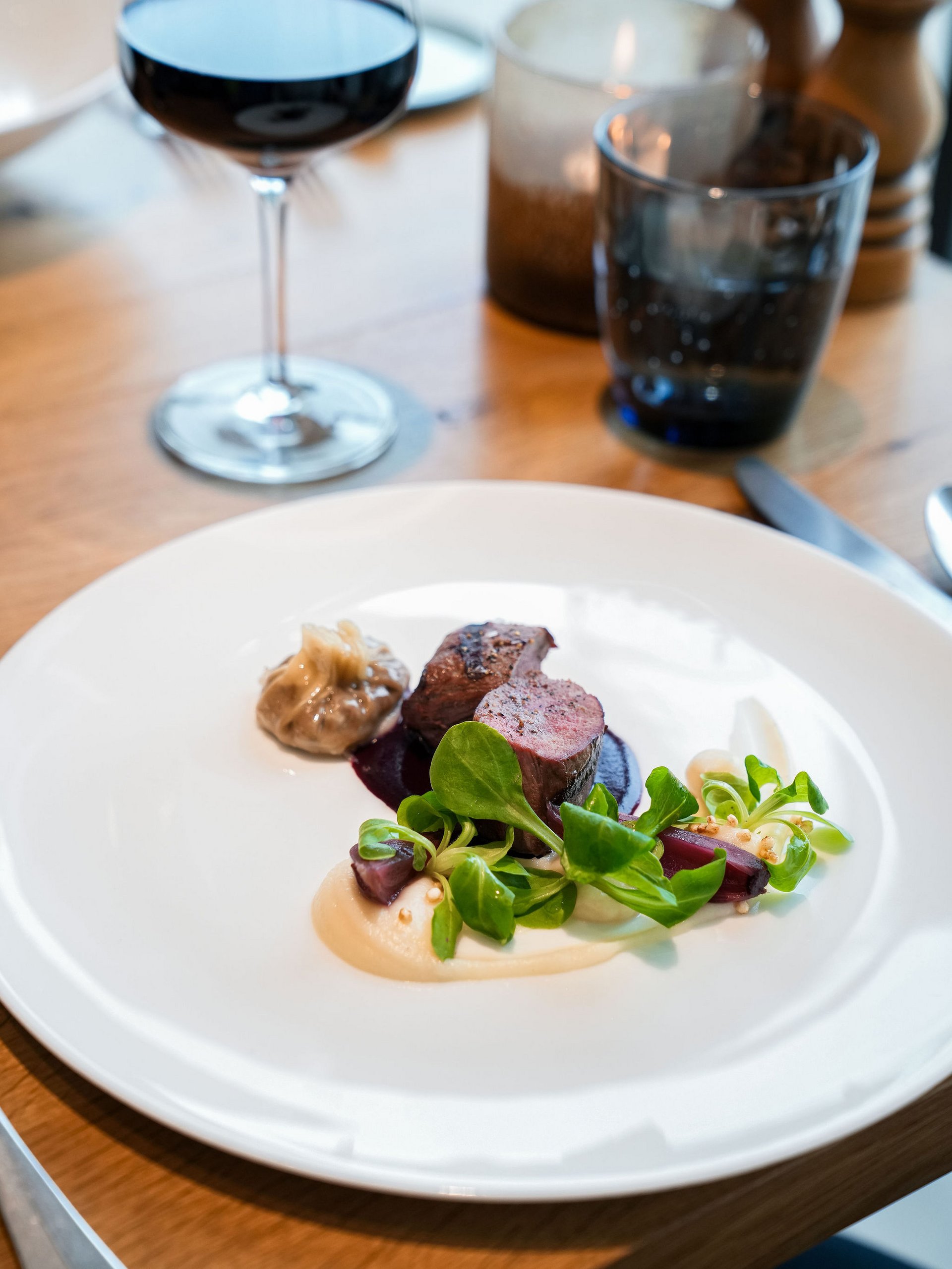 Seezeitlodge : Galerie photos Plat raffiné avec viande, sauce, salade verte et verre de vin rouge en arrière-plan