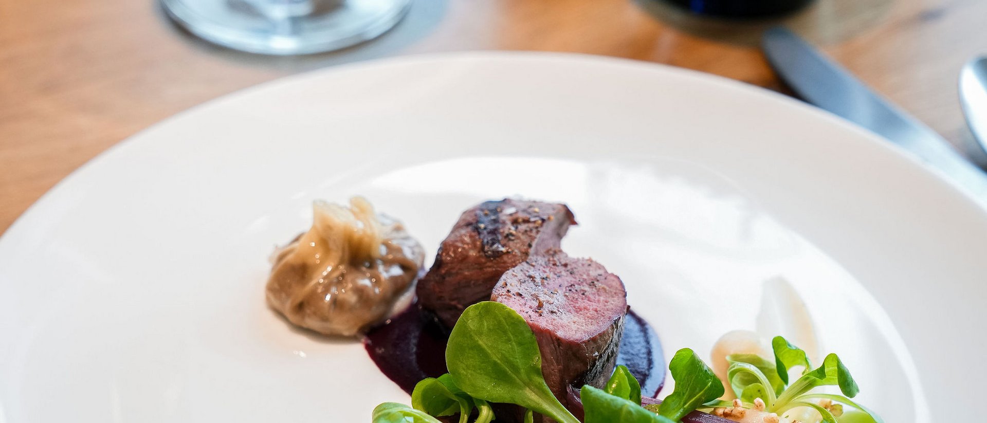 Seezeitlodge : Galerie photos Plat raffiné avec viande, sauce, salade verte et verre de vin rouge en arrière-plan