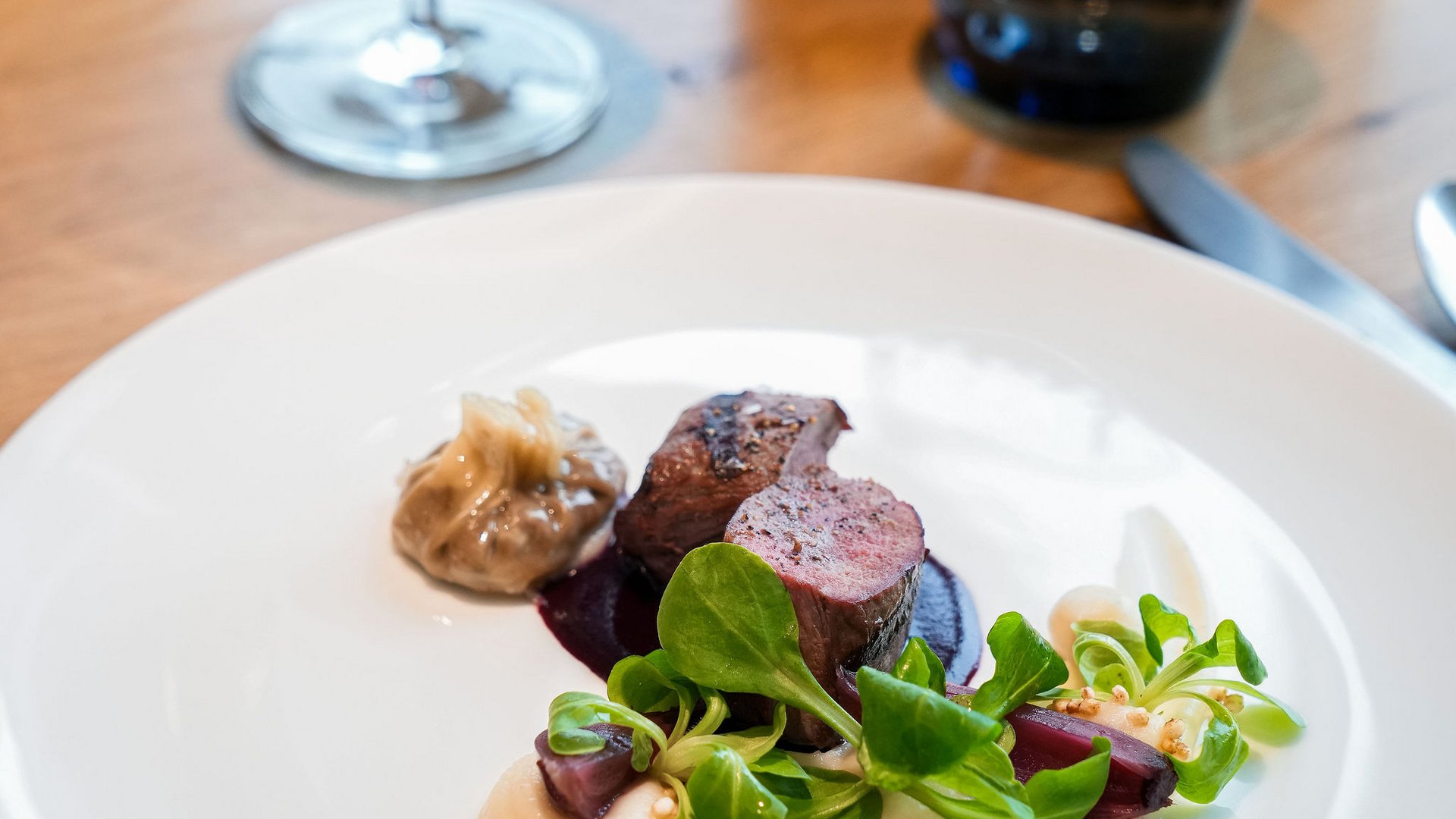 Seezeitlodge: Bildergalerie Elegantes Gericht mit Fleisch, Sauce, grünem Salat und Rotwein im Hintergrund