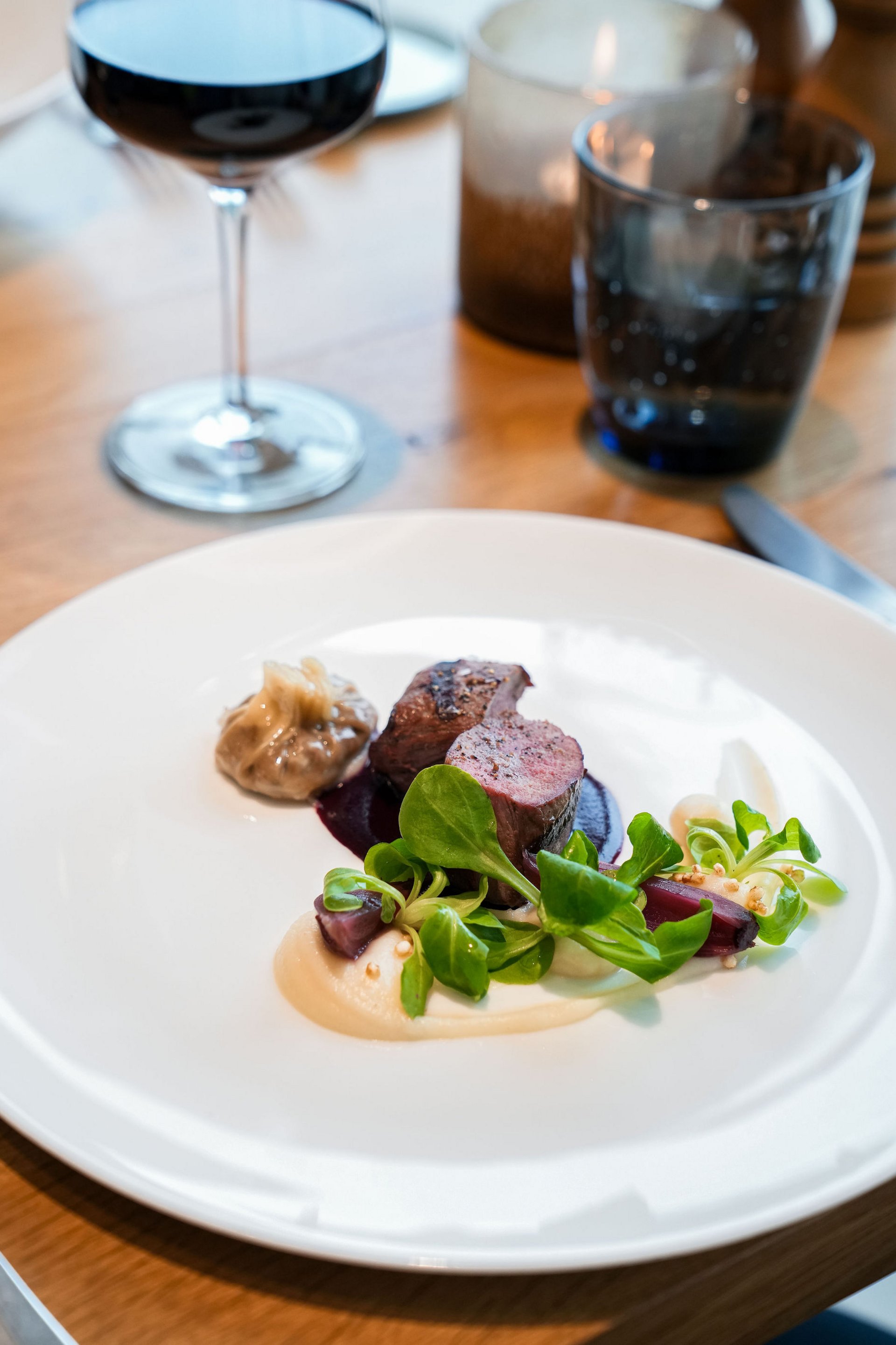 Seezeitlodge : Galerie photos Plat raffiné avec viande, sauce, salade verte et verre de vin rouge en arrière-plan