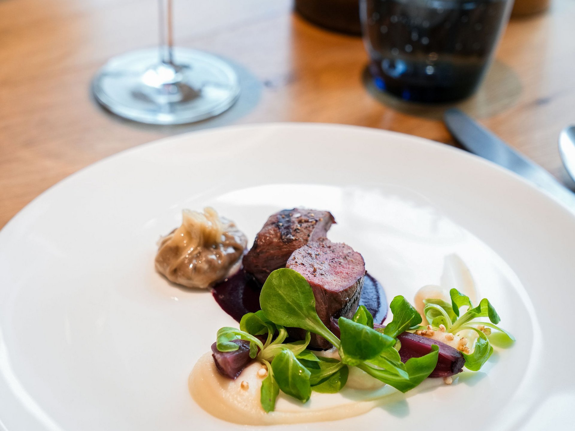 Seezeitlodge: Bildergalerie Elegantes Gericht mit Fleisch, Sauce, grünem Salat und Rotwein im Hintergrund