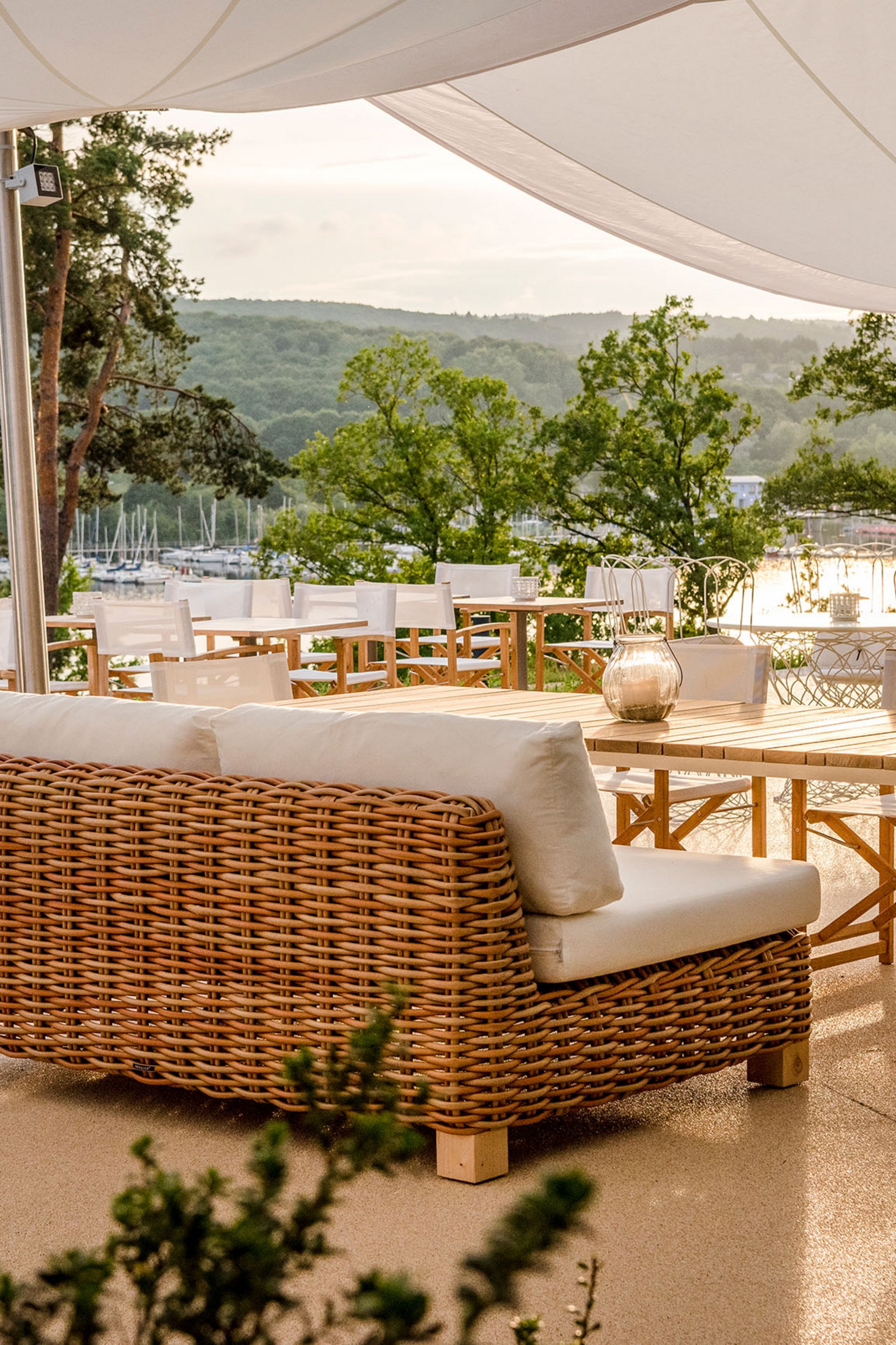 Seezeitlodge: Bildergalerie Terrasse mit Rattanmöbeln und Blick auf einen See und grüne Hügel