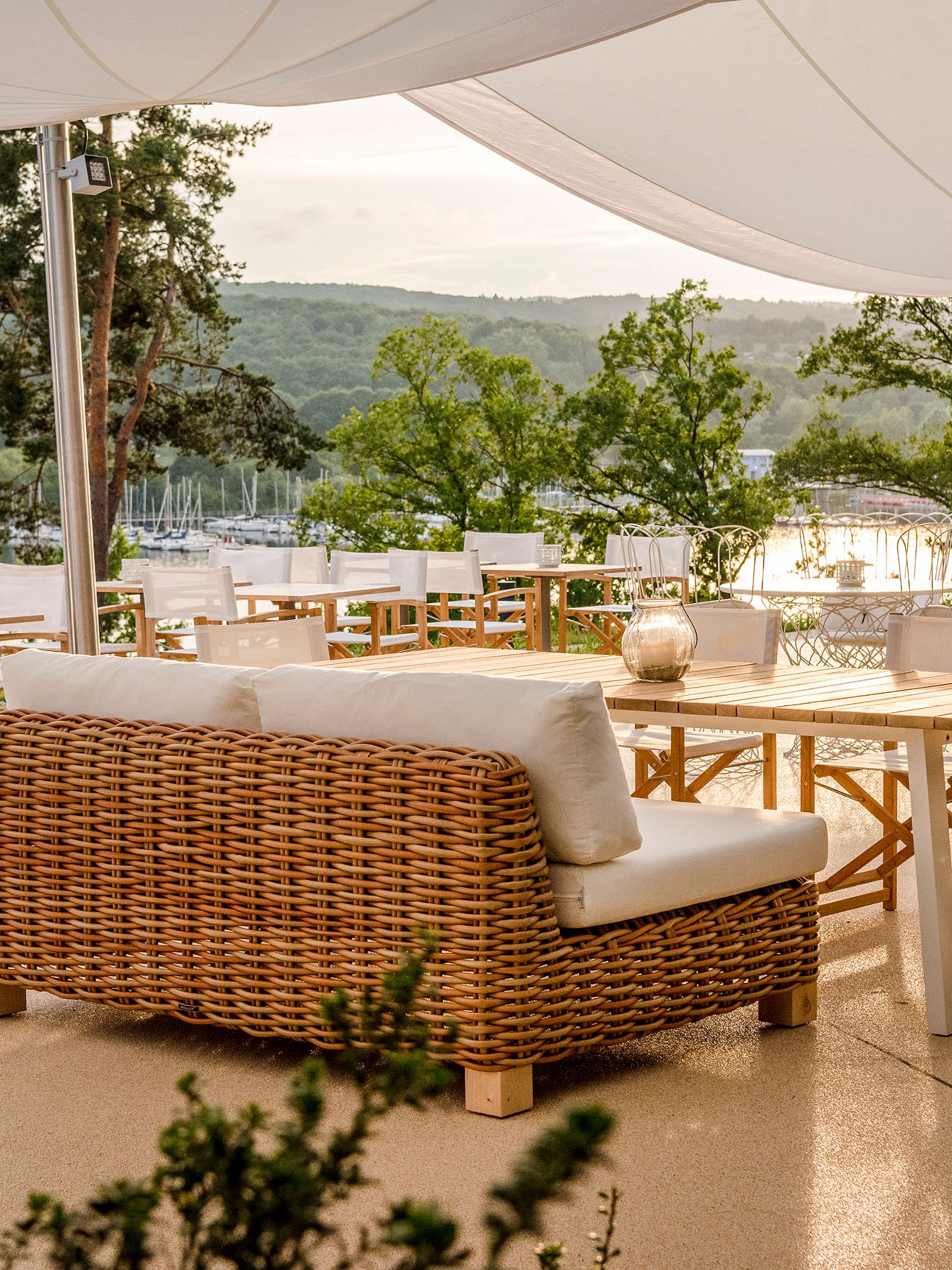 Seezeitlodge: Bildergalerie Terrasse mit Rattanmöbeln und Blick auf einen See und grüne Hügel
