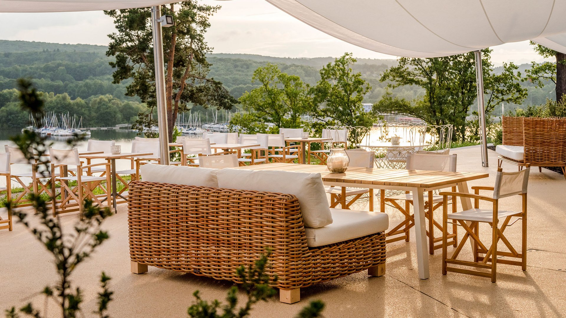 Seezeitlodge : Galerie photos Terrasse avec meubles en rotin et vue sur un lac et des collines verdoyantes