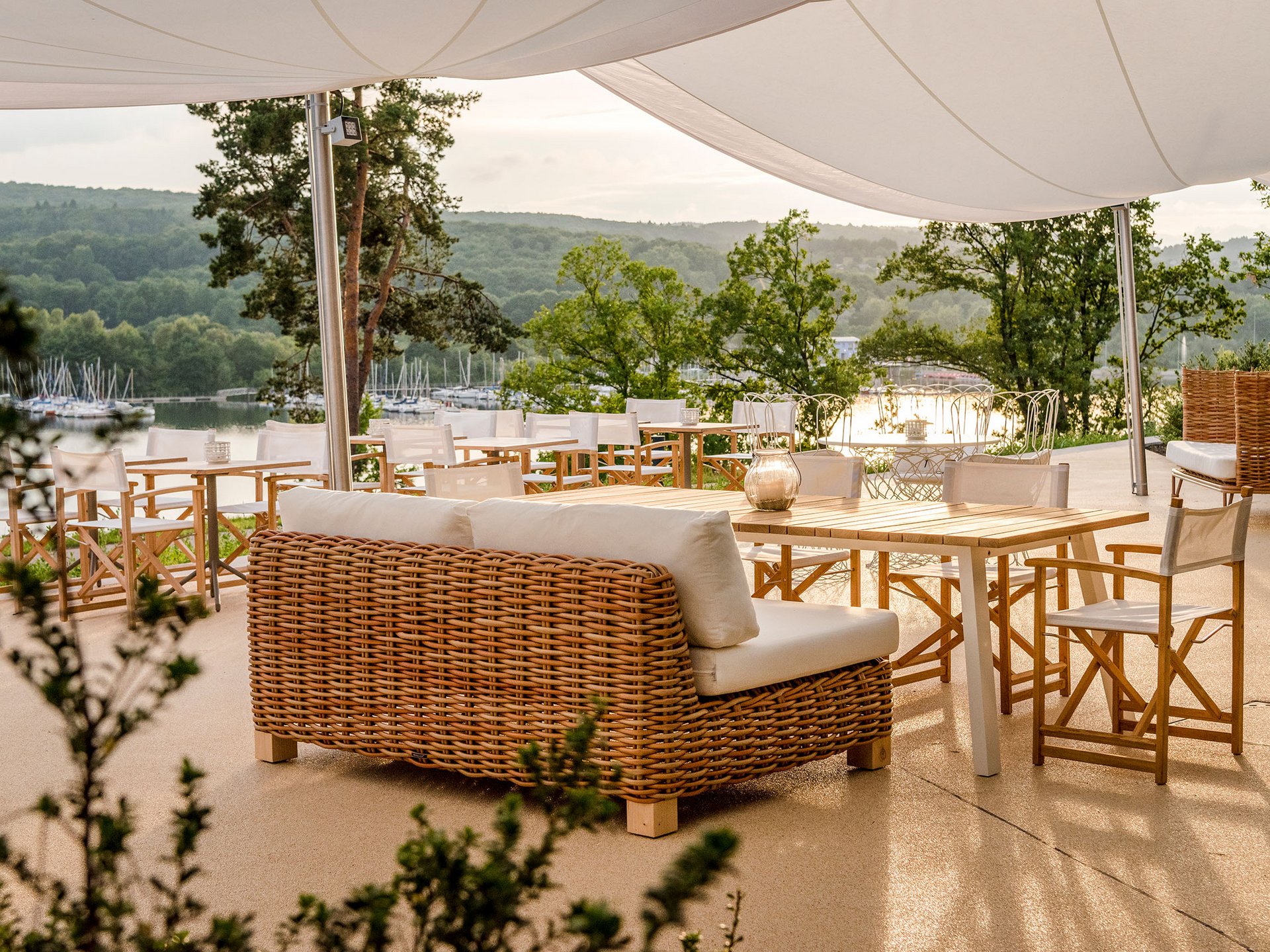 Seezeitlodge : Galerie photos Terrasse avec meubles en rotin et vue sur un lac et des collines verdoyantes