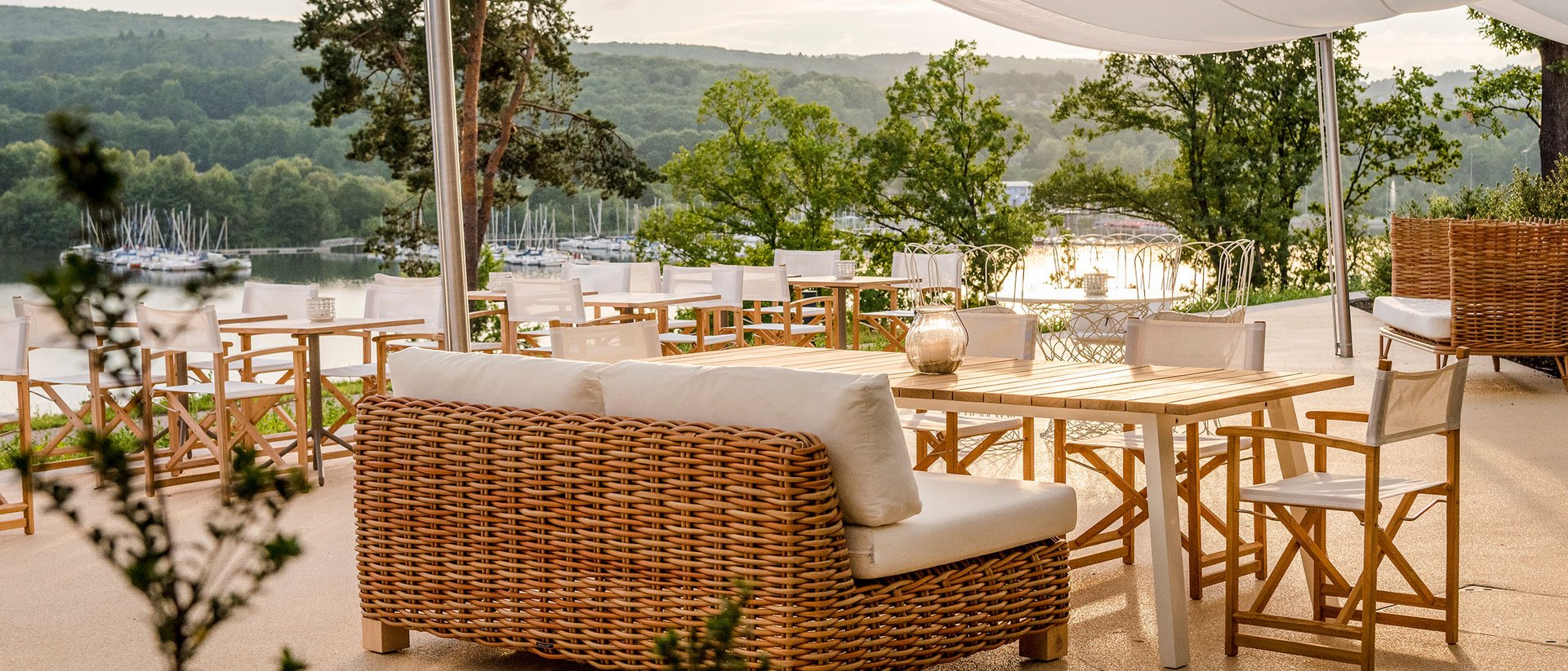 Seezeitlodge : Galerie photos Terrasse avec meubles en rotin et vue sur un lac et des collines verdoyantes