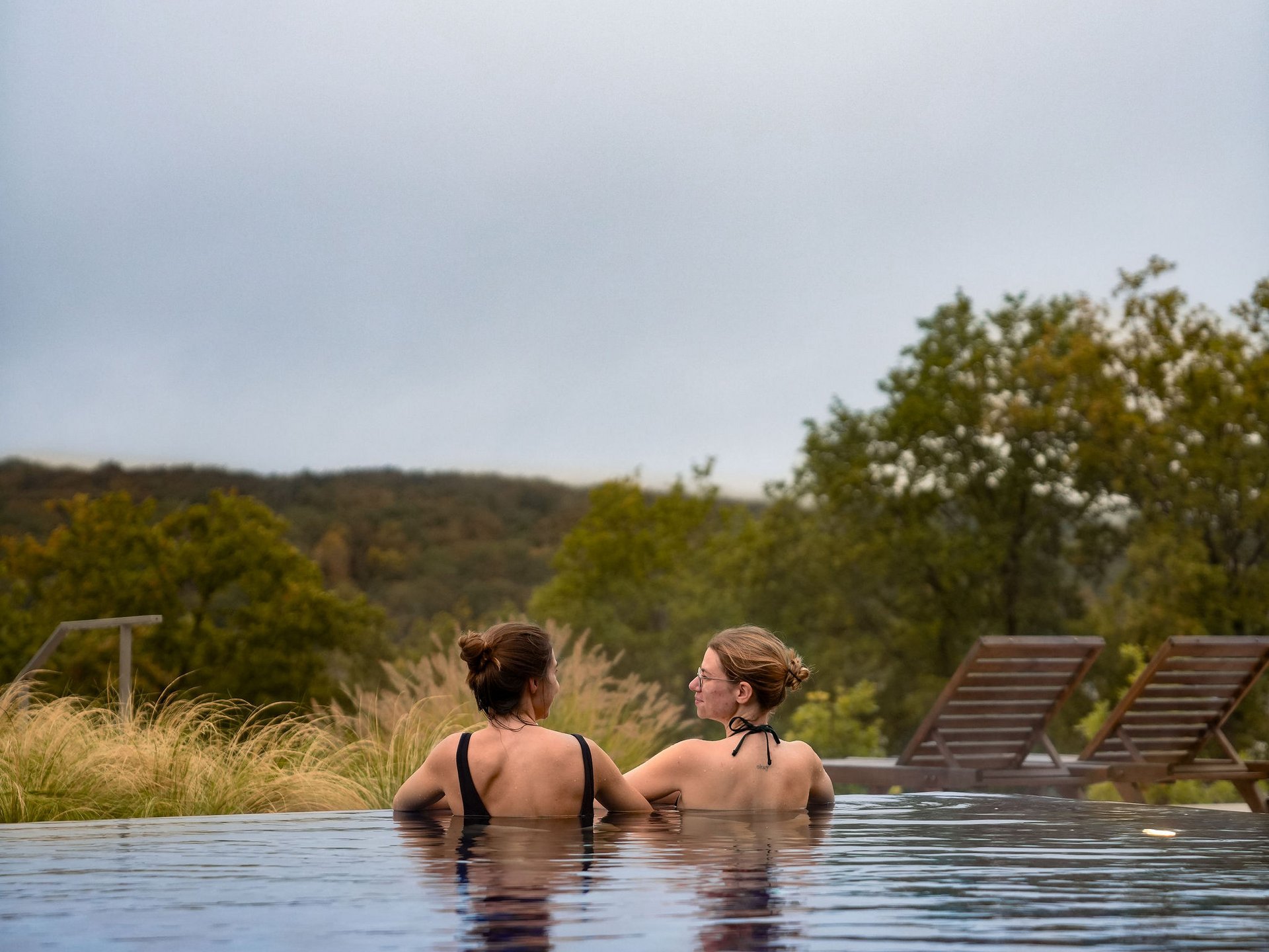 Le Seezeitlodge : votre hôtel au lac de Bostal Deux femmes dans une piscine avec vue sur la nature verte et des chaises longues