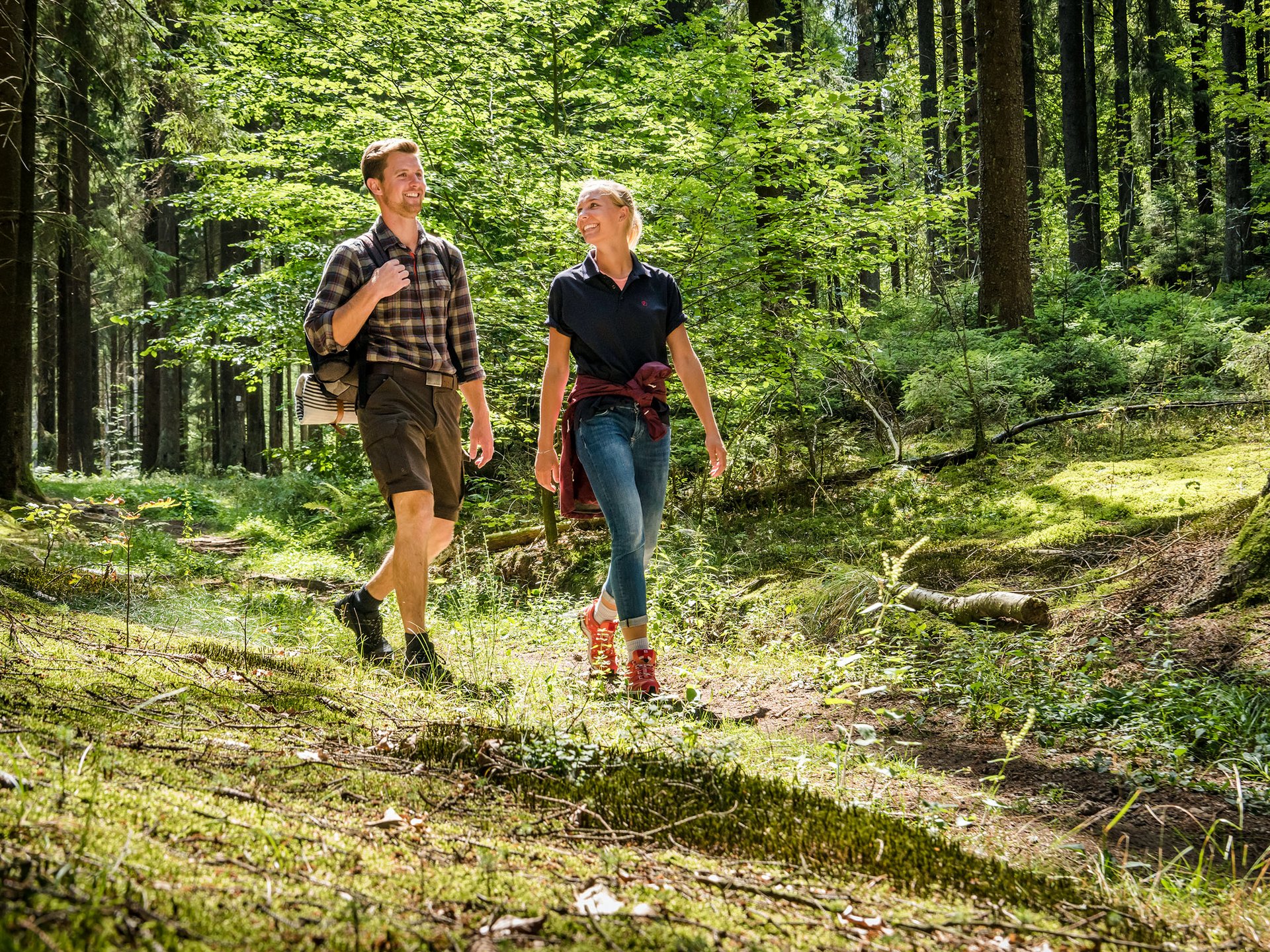 Ihr Wellnesshotel mit Yoga in Deutschland Paar wandert fröhlich auf einem sonnigen Waldweg