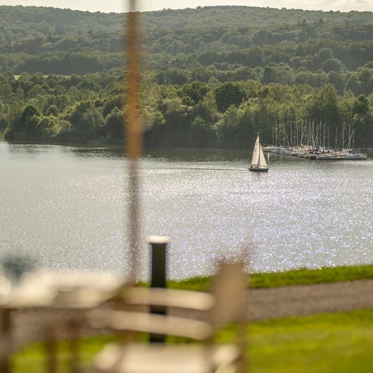 Ihr Kraftort in Deutschland Segelboot auf funkelndem See mit Wald und Yachthafen im Hintergrund