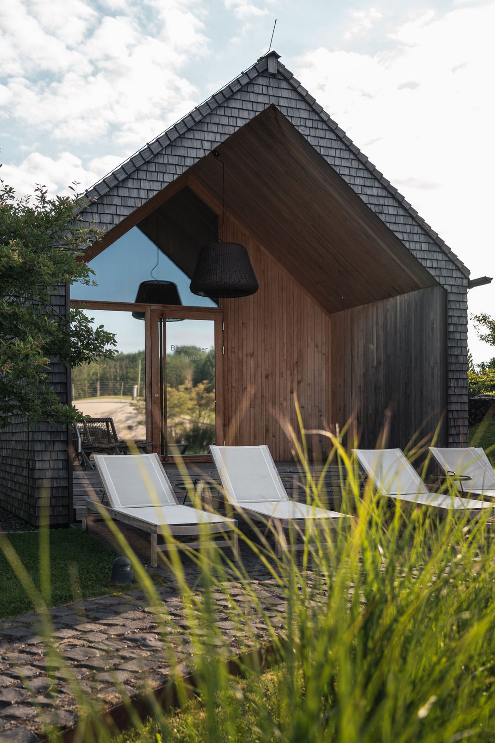 Seezeitlodge : Galerie photos Sauna moderne avec chaises longues devant une façade en bois sous un ciel nuageux