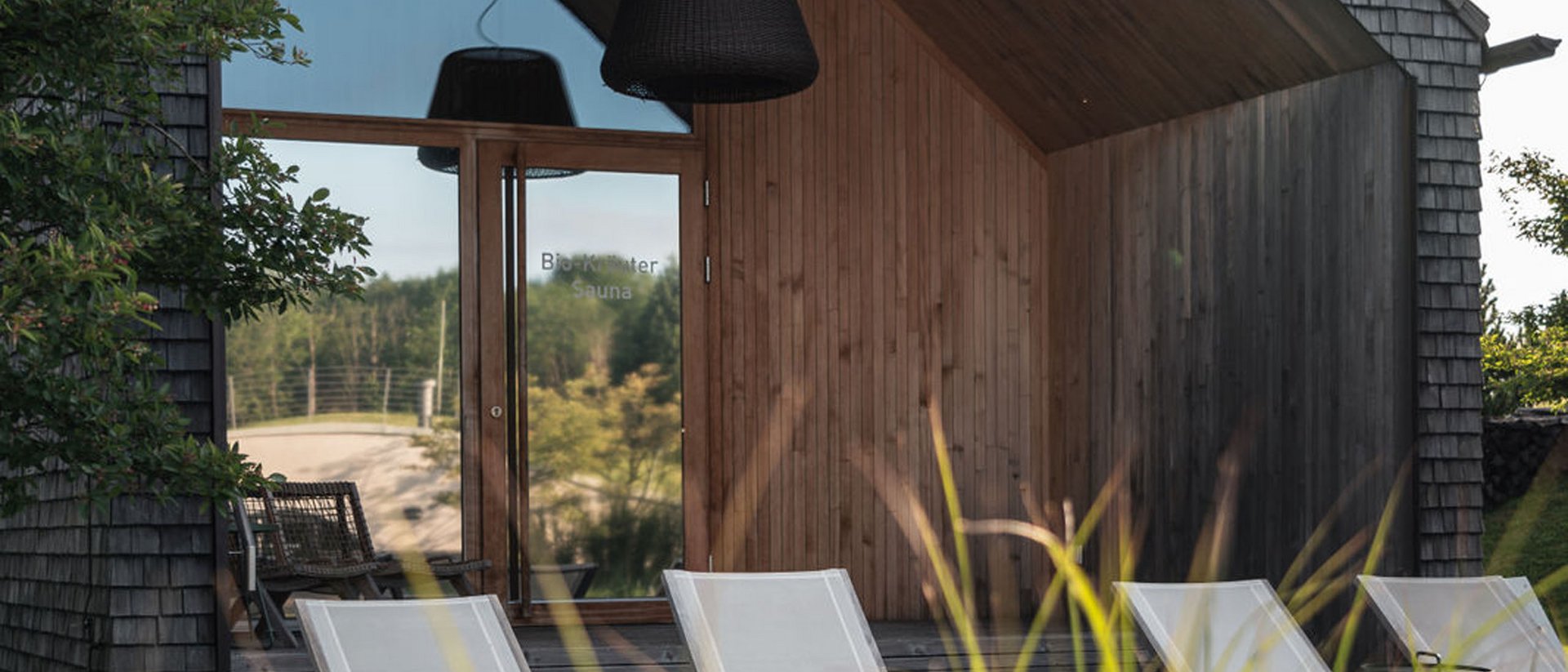 Seezeitlodge : Galerie photos Sauna moderne avec chaises longues devant une façade en bois sous un ciel nuageux