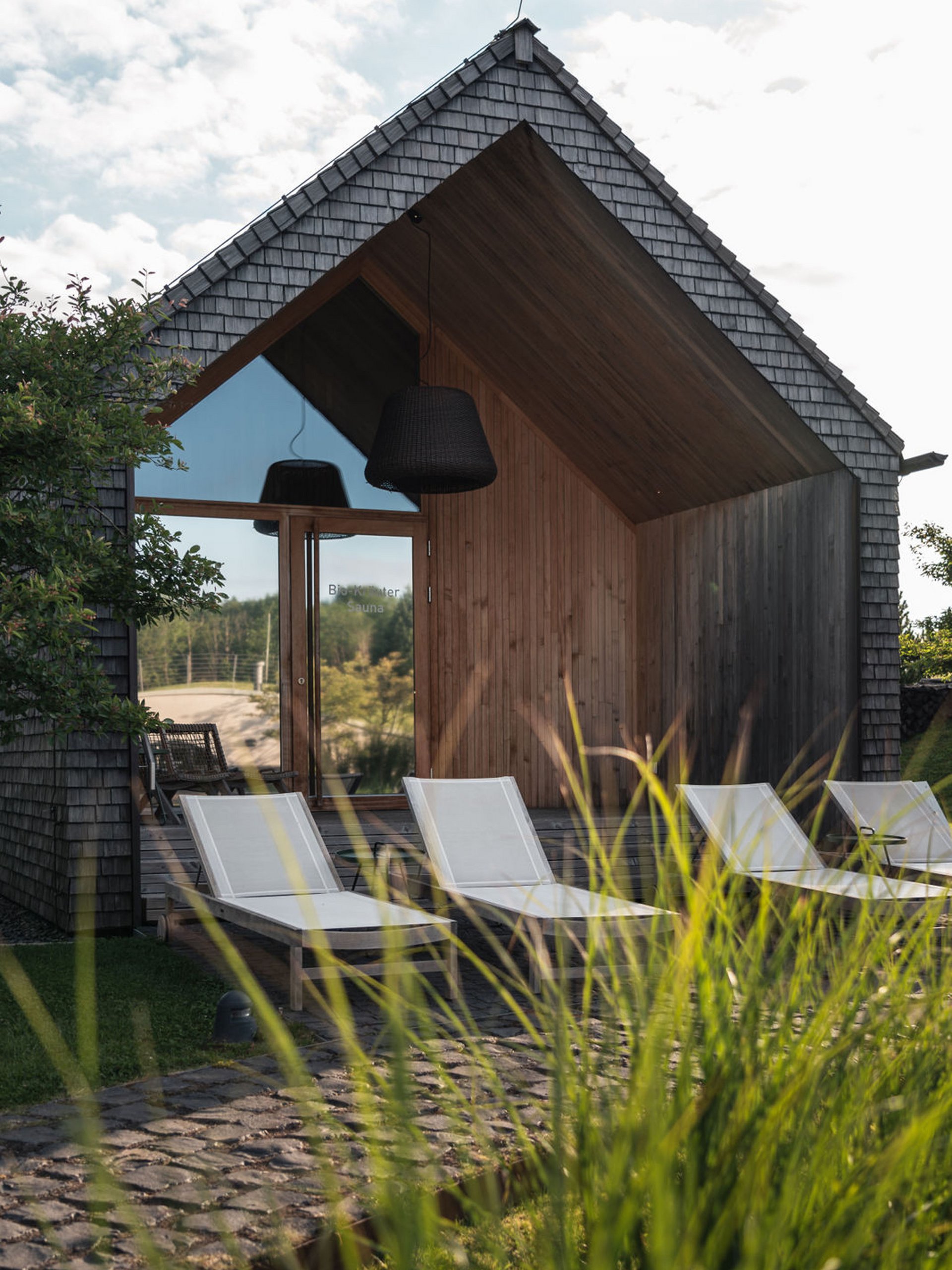 Seezeitlodge : Galerie photos Sauna moderne avec chaises longues devant une façade en bois sous un ciel nuageux