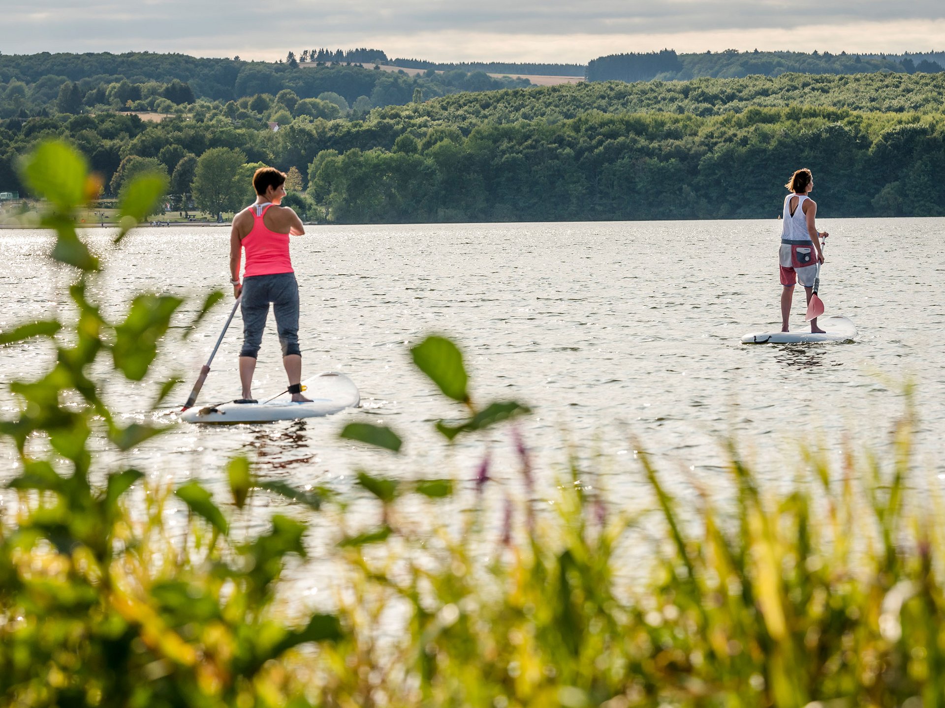 Ihr Wellnesshotel mit Yoga in Deutschland Zwei Frauen beim Stand-up-Paddling auf einem See umgeben von Wald