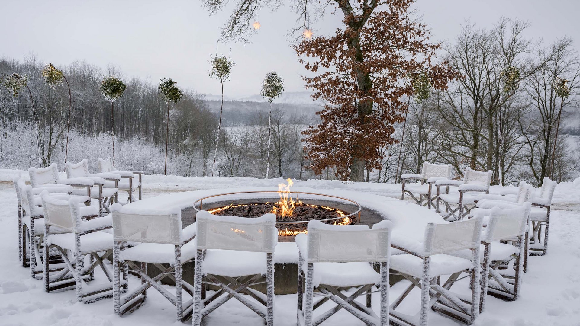 Die Seezeitlodge: Ihr Hotel am Bostalsee Verschneite Sitzgruppe mit Stühlen um eine brennende Feuerschale vor winterlicher Waldkulisse