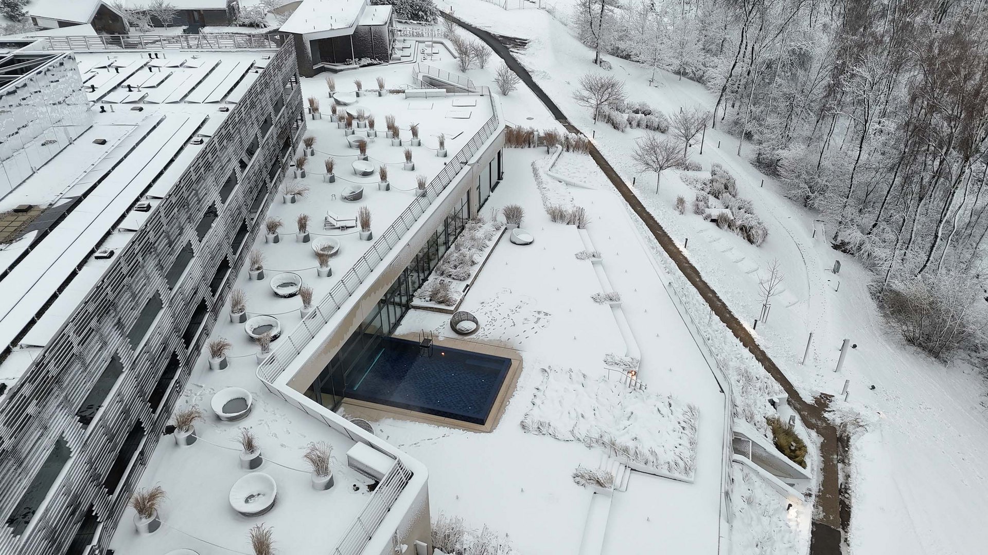 Die Seezeitlodge: Ihr Hotel am Bostalsee Luftaufnahme eines schneebedeckten Hotelgebäudes mit Außenpool und winterlichem Wald