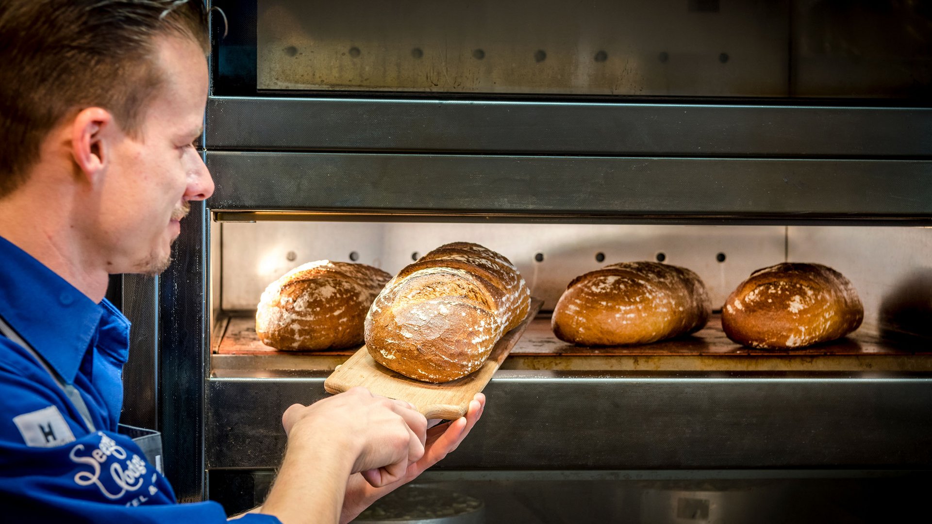 Seezeitlodge: Backstube und Patisserie Bäcker holt frisch gebackenes Brot aus dem Ofen