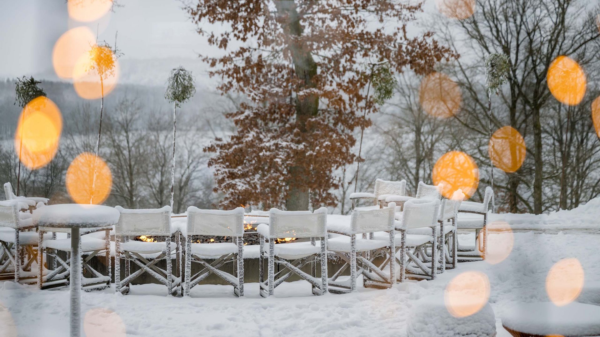 Die Seezeitlodge: Ihr Hotel am Bostalsee Verschneite Terrasse mit weißen Stühlen, Tischen und kleinen Feuern vor kahlen Bäumen