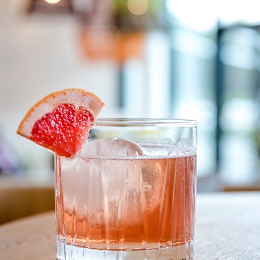 Ihr Genusshotel am Bostalsee Cocktail mit Eis und Grapefruitecke auf Holzoberfläche