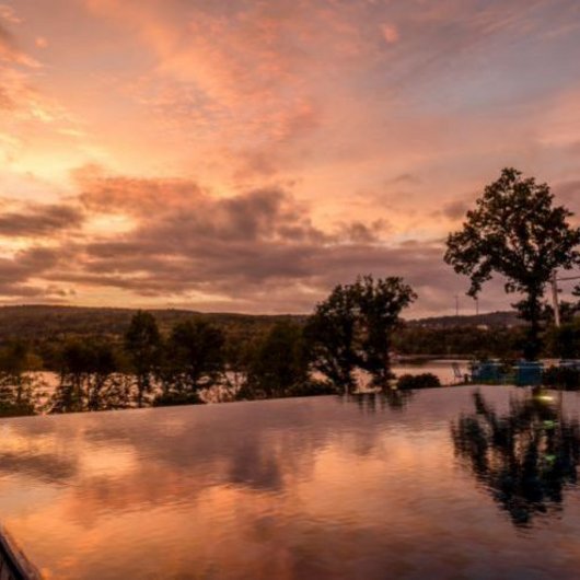 Seezeitlodge: Ihr Spa-Hotel am Bostalsee Unendlich-Pool bei Sonnenuntergang mit Spiegelung und Bäumen im Hintergrund