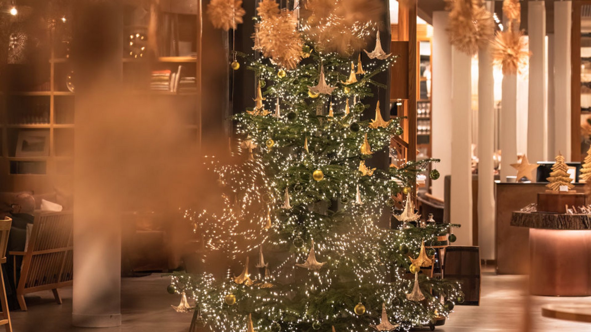 Seezeitlodge: Lieblingsgeschichten Weihnachtsbaum mit goldenen Ornamenten und Lichtern in einem modern dekorierten Raum