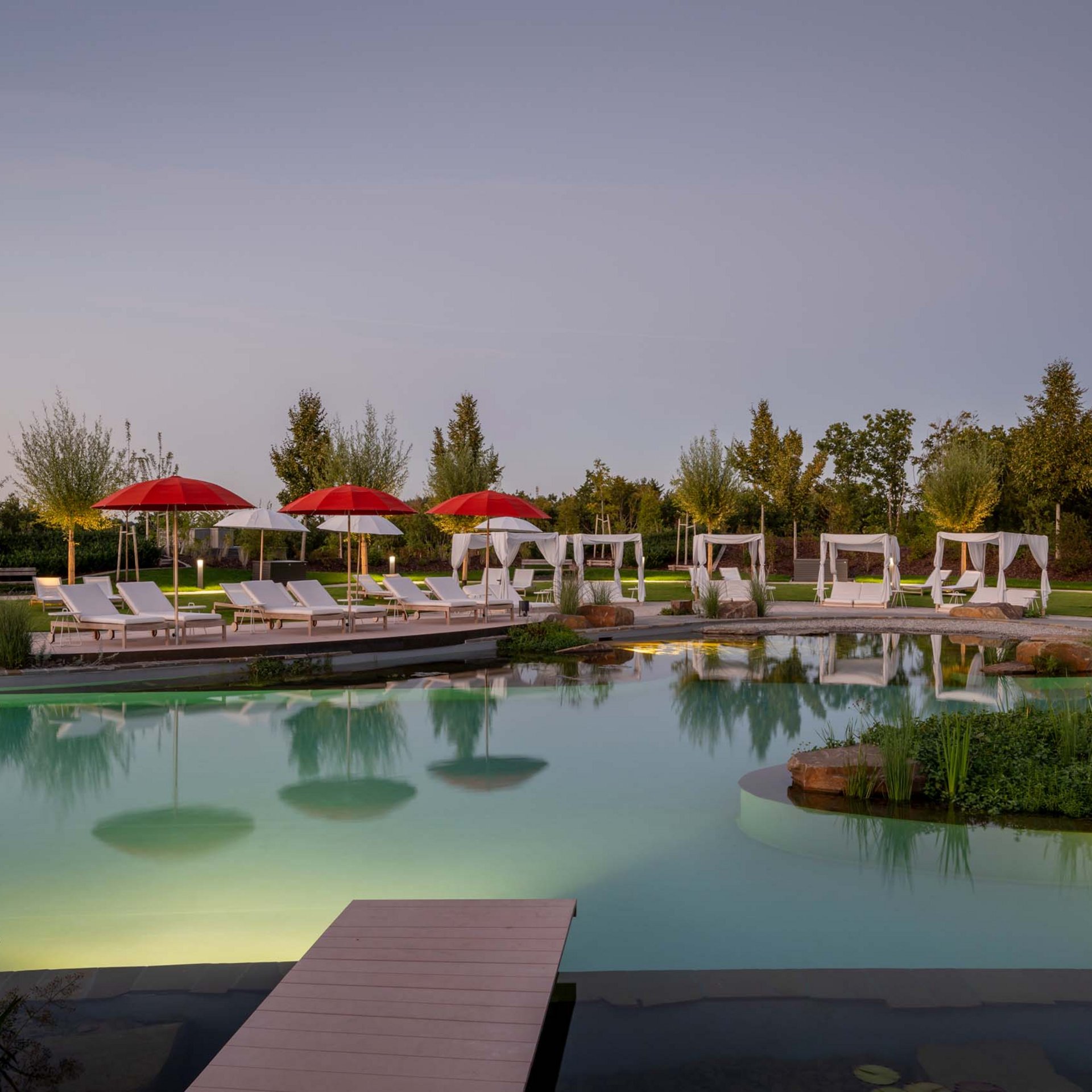 Le Seezeitlodge : votre hôtel au lac de Bostal Vue au crépuscule d'une piscine avec parasols rouges et blancs et chaises longues
