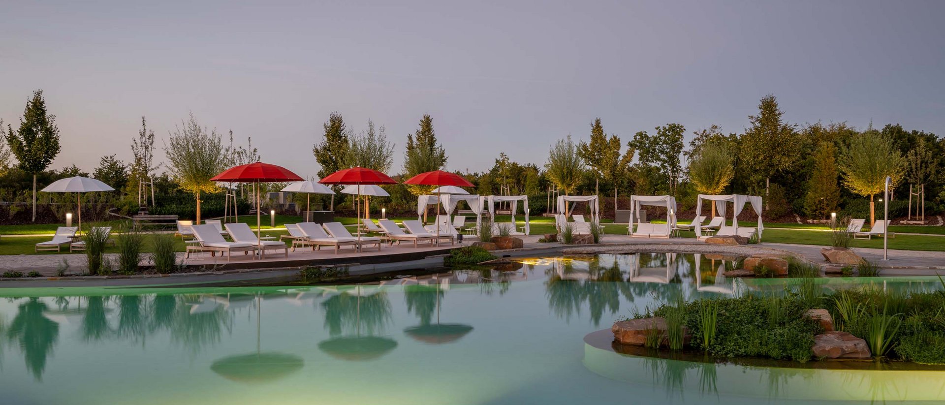 Seezeitlodge: Ihr Wellnesshotel am Bostalsee für pure Erholung Abendblick auf einen beleuchteten Pool mit roten und weißen Sonnenschirmen und Liegestühlen