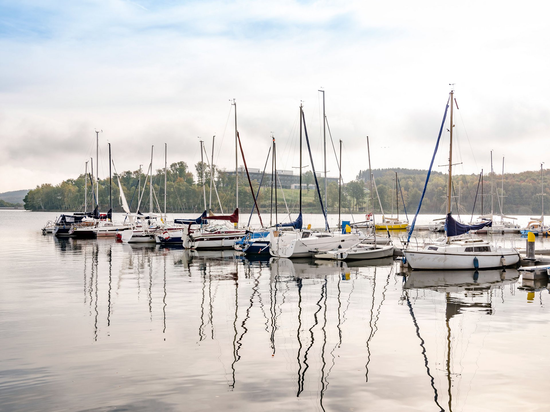 Urlaub am Bostalsee: die Highlights der Region Segelboote im Hafen auf ruhigem See vor bewaldetem Ufer