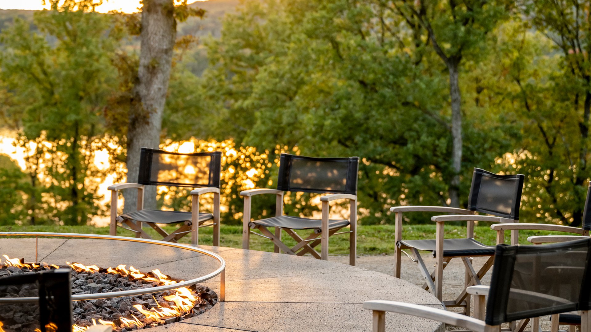 Seezeitlodge: Lieblingsgeschichten Runde Feuerschale mit Stühlen draußen vor Bäumen bei Sonnenuntergang