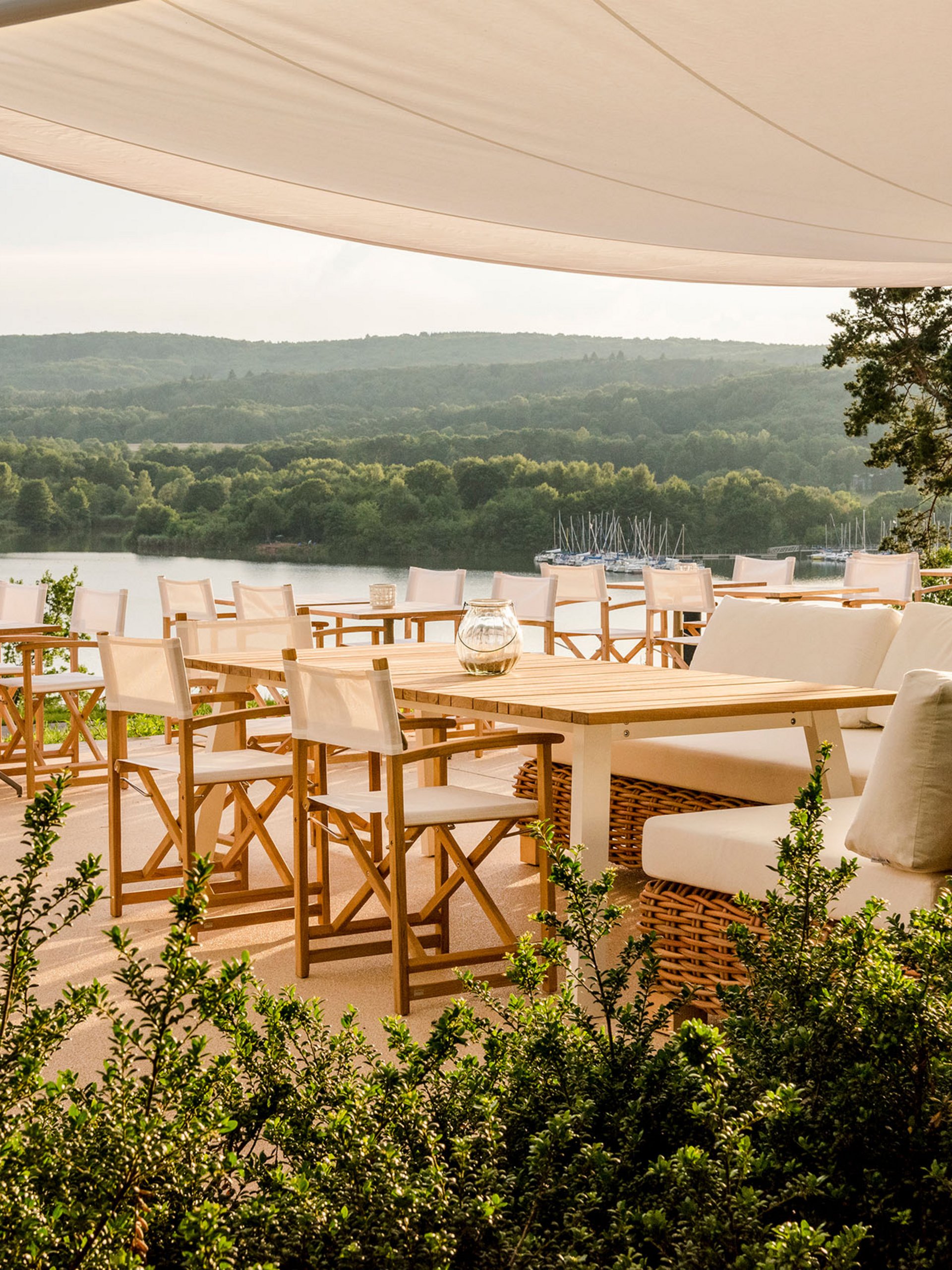 Seezeitlodge: Bildergalerie Sonnenterrasse mit weißen Stühlen und Seenblick unter einem Sonnensegel