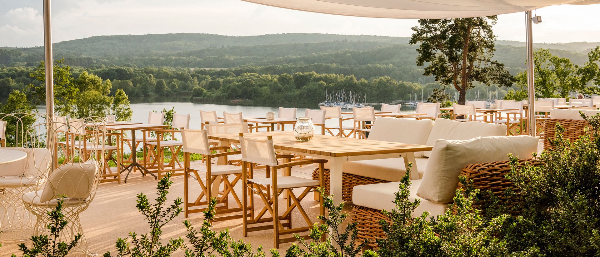 Seezeitlodge: Bildergalerie Sonnenterrasse mit weißen Stühlen und Seenblick unter einem Sonnensegel
