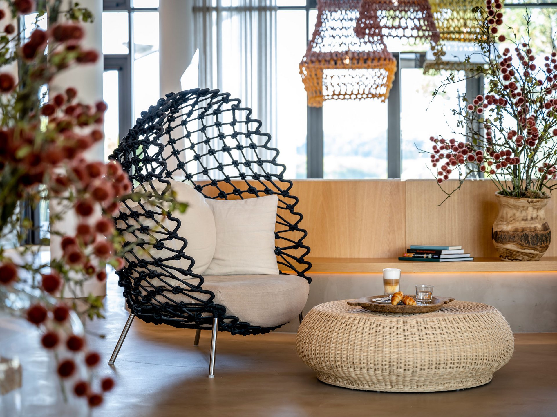 Seezeitlodge: Bildergalerie Moderner Sitzbereich mit Korbtisch, schwarzem Sessel und Blumen in einer hellen Lounge