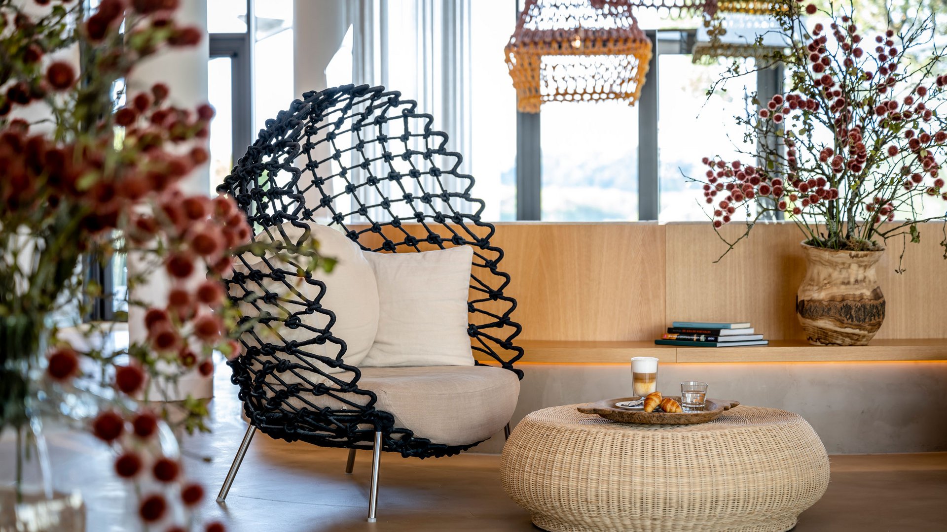 Seezeitlodge : Galerie photos Espace salon moderne avec fauteuil noir, table en rotin et fleurs dans un salon lumineux