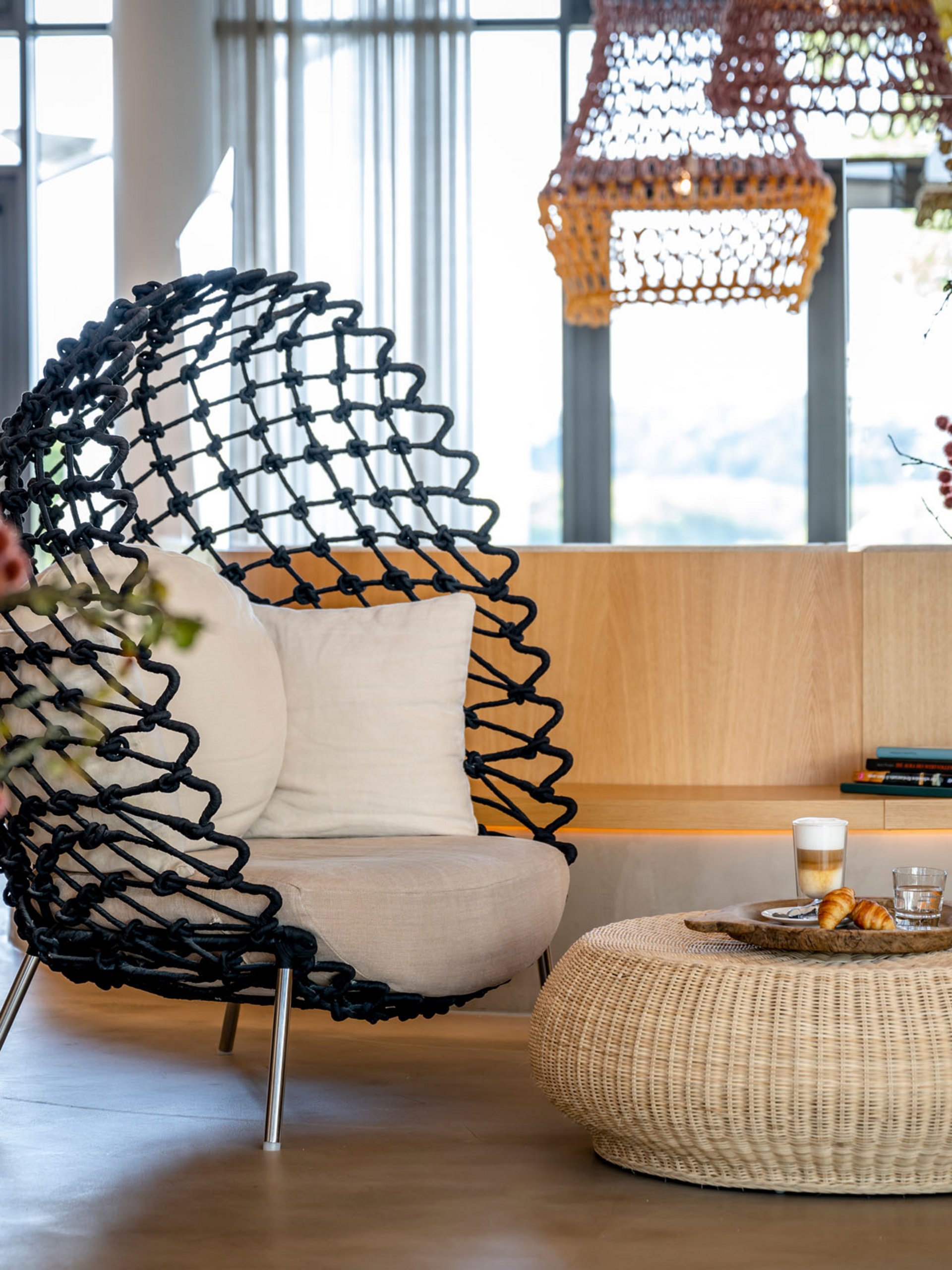 Seezeitlodge : Galerie photos Espace salon moderne avec fauteuil noir, table en rotin et fleurs dans un salon lumineux