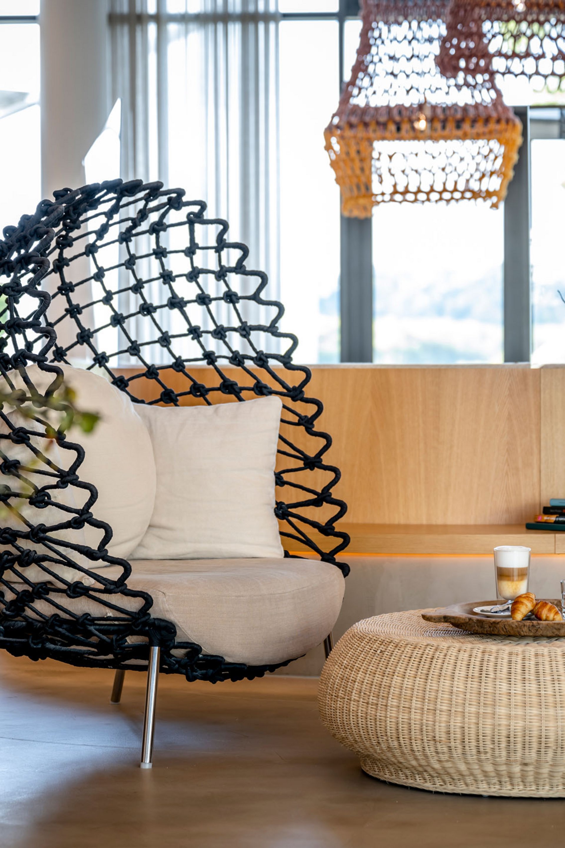 Seezeitlodge: Bildergalerie Moderner Sitzbereich mit Korbtisch, schwarzem Sessel und Blumen in einer hellen Lounge