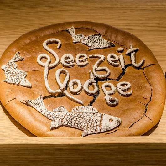 Seezeitlodge: Backstube und Patisserie Brot mit Aufschrift Seezeit Lodge und Fischmotiven auf einem Holzregal