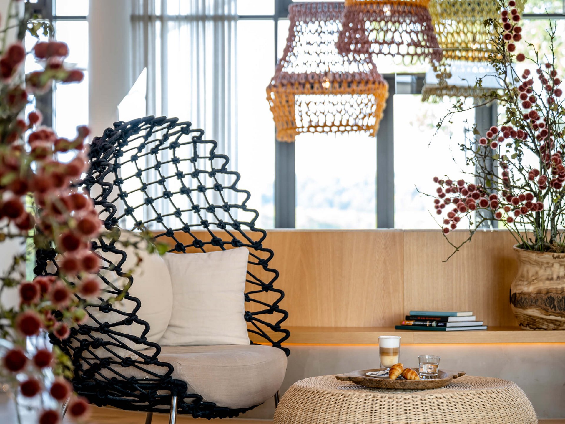 Le Seezeitlodge : votre hôtel au lac de Bostal Espace de vie moderne avec chaise en osier, ottomane et décorations sous lumière naturelle