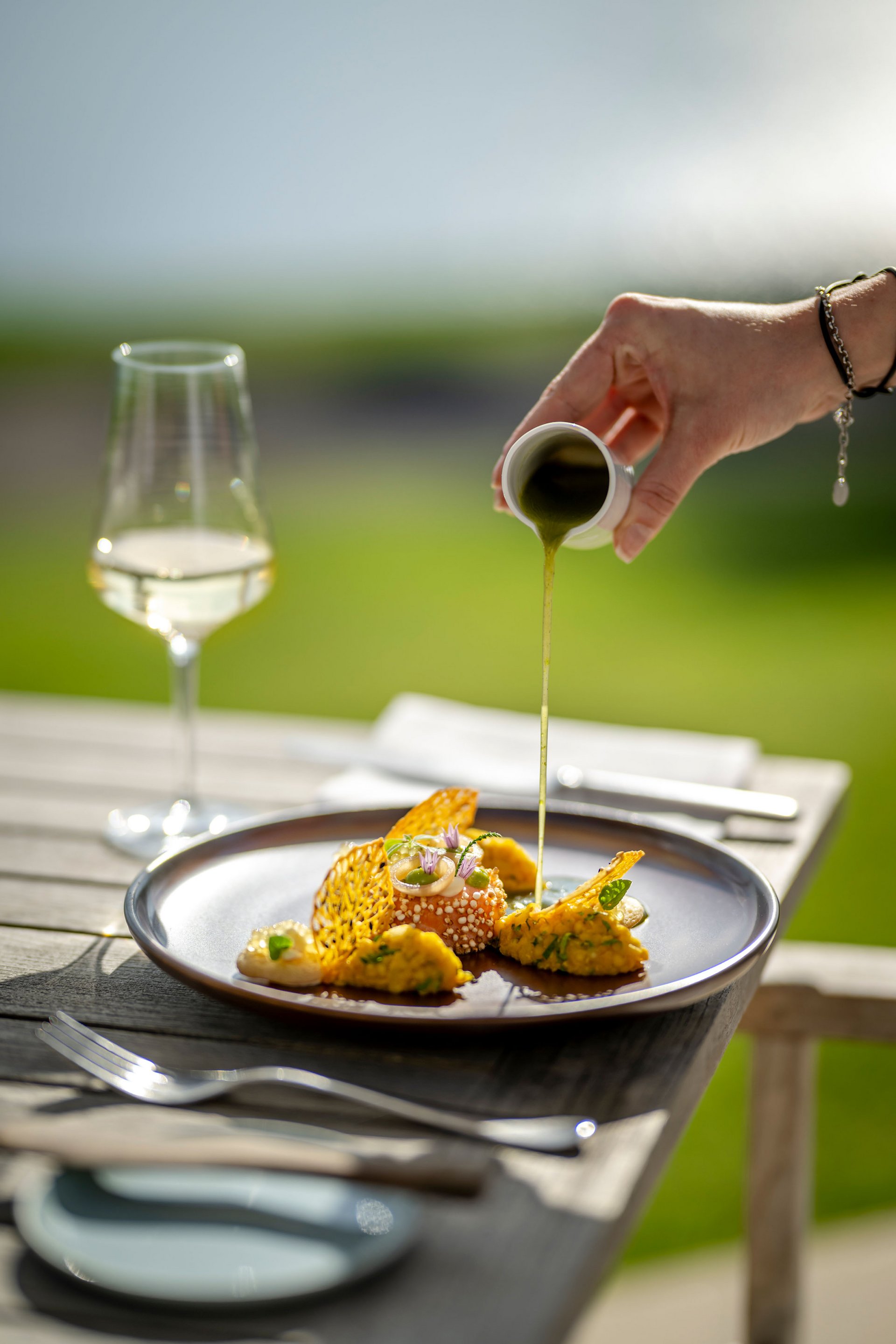 Seezeitlodge : Galerie photos Main verse une sauce verte sur un plat gastronomique artistiquement présenté en extérieur